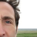 photo showing a partial part of a mans face with green fields in the background