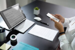 Photo of a person capturing a document using a mobile phone with a tablet sitting on a desk