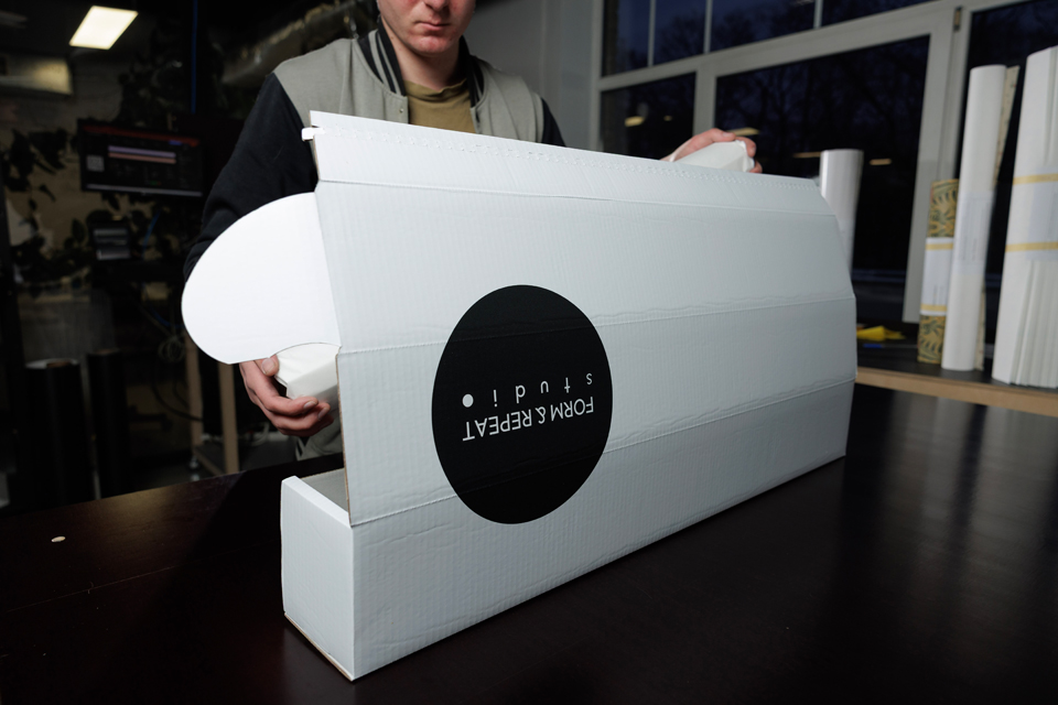 Worker packing a roll of wallpaper into a branded shipping box